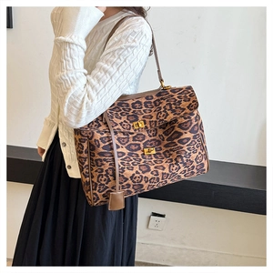 Detail of leopard print tote bag featuring a golden twist lock and brown leather strap