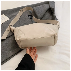 Close-up of cream PU leather moon bag with adjustable wide strap on grey wool background