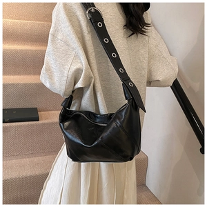 Close-up of black hobo bag with wide shoulder strap featuring metallic silver eyelets