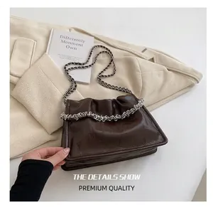Detail of dark brown glossy wrinkled cloud bag with silver chain straps on a beige blazer