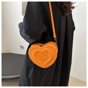 Detail of a bright orange heart-shaped crossbody bag with embossed texture and metal zipper