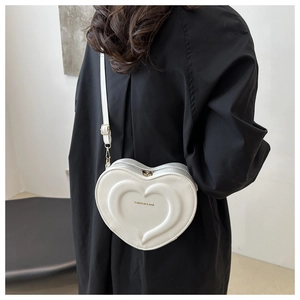 Detail of white heart-shaped crossbody bag with embossed texture and gold lettering