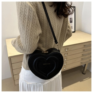 Model wearing a black heart-shaped crossbody bag with gold zippers and fashion lettering