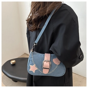 Dettaglio borsa a spalla in denim blu con finiture rosa, ciondoli a stella e fibbia argento