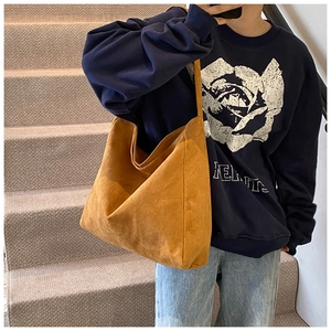 Close-up of a mustard yellow suede tote bag with wide straps on a minimalist model
