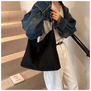 Minimalist large black nylon tote bag shown as casual shoulder bag on model in stairwell