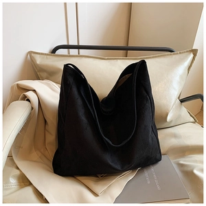 Detail of large black matte canvas tote bag styled on a cream leather chair with books