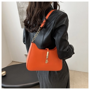Model wearing orange crescent shoulder bag with golden chain and metallic buckle