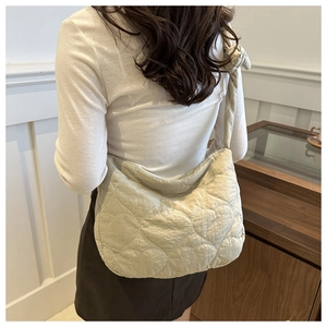 Detail of cream nylon dumpling bag featuring heart quilting and decorative knot strap