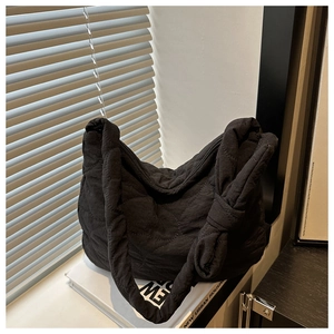 Detail of black quilted nylon hobo bag featuring a decorative side bow on white books