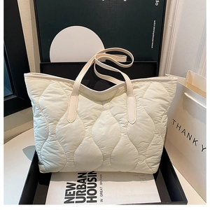 Detail of off-white wave-quilted puffer tote bag arranged with elegant book props