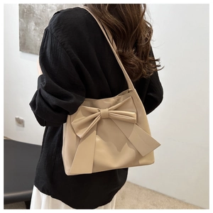 Close-up of stylish beige tote bag featuring a large decorative bow and matte leather finish