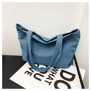 Close-up of blue denim tote bag with textured fabric, long handles and zipper closure
