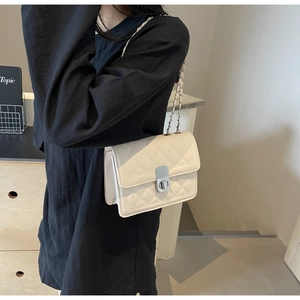 Dettaglio borsa trapuntata beige con catena e chiusura argento su maglione nero