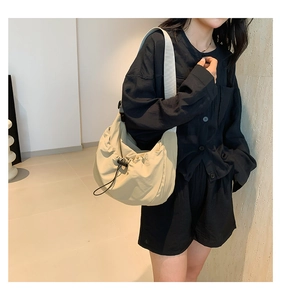 Detailed view of beige pleated cloud bag with grey strap worn by a model in black outfit