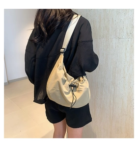 Detail of a beige nylon drawstring shoulder bag with adjustable strap worn by a model