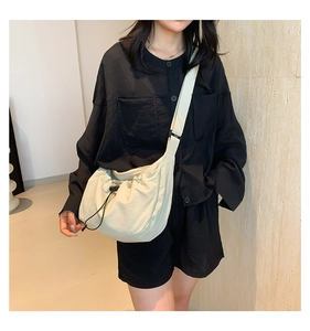 Detail of cream drawstring crossbody bag featuring soft pleated nylon and a wide strap