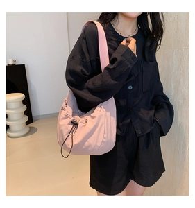 Detail of light pink drawstring crossbody bag with pleated fabric texture on a model