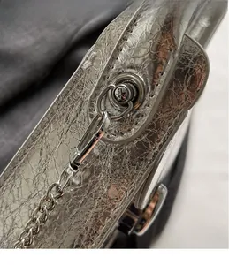 Detail of silver metallic bag with wrinkled texture, metal hook, and chain strap