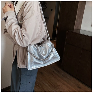 Silver metallic pleated shoulder bag with chunky chain strap worn by a model