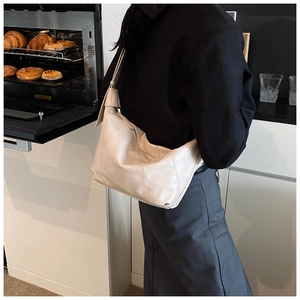 Chic beige hobo bag styled as an underarm shoulder bag on a model in a kitchen setting