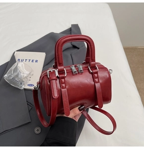 Top view of wine red Boston bag on a bed with a blazer and decorative book