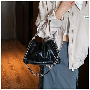 Detail of black glossy oil wax leather handbag with silver chain on model indoors