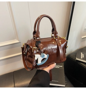 Dettaglio di una borsa Boston marrone lucida con trama in pelle, manico e ciondolo