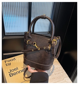 Détail du sac seau marron foncé avec ferrures dorées et bandoulière réglable sur pierre