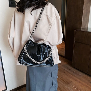 Chic black pleated cloud bag with silver chain straps worn by a model in a modern interior