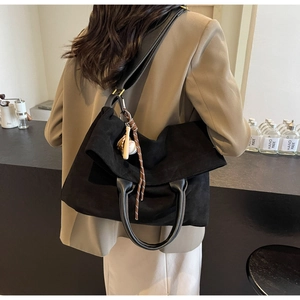 Dettaglio di una borsa tote grande in camoscio nero con manici in pelle e ciondolo da baseball