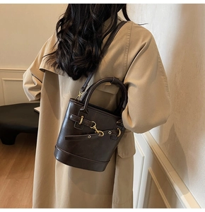 Détail d'un sac seau rétro en cuir marron foncé porté sur un trench-coat beige