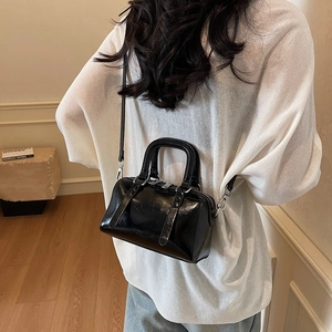 Glossy black mini Boston bag with silver hardware worn as a crossbody on a model