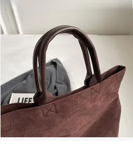 Dettaglio dei manici rinforzati e del tessuto scamosciato sulla borsa tote marrone