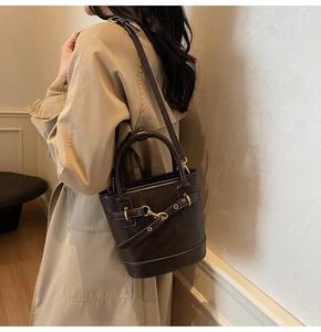 Détail du sac seau marron foncé avec boucles dorées et bandoulière porté par un modèle