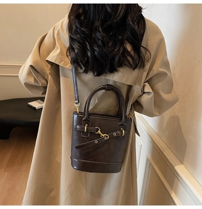 Détail du sac seau marron foncé avec boucles dorées et décorations de lanières en cuir