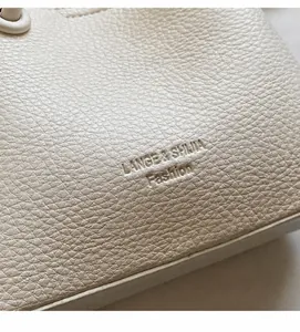 Detail of lychee grain leather texture and embossed logo on minimalist bucket bag