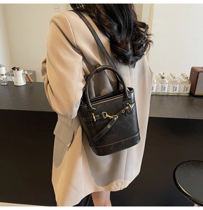 Détail d'un sac seau vintage noir avec boucles dorées porté par un mannequin en café