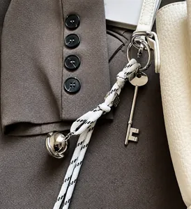 Detail of black and white woven rope keychain with silver bell and key pendant on a bag
