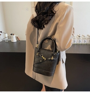 Détail d'un sac seau noir avec boucle dorée et bandoulière porté par un mannequin
