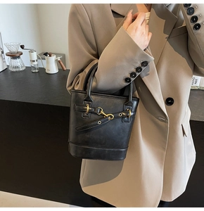 Détail d'un sac seau vintage en cuir noir avec boucles dorées dans un café chic