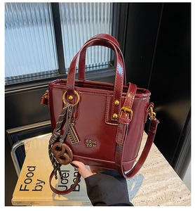 Detail of burgundy patent leather mini tote with gold hardware and logo on books