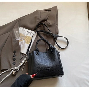 Detail of black lychee grain bucket bag with logo and decorative braided tassel charm