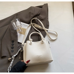 Detail of white lychee leather bucket bag with metal rings and woven charm