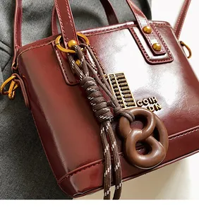 Detail of burgundy glossy leather handbag with golden abacus and woven cord pendant charms