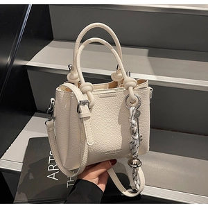 Detail of white lychee-patterned bucket bag with decorative scarf on grey steps