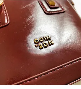 Close-up of glossy dark burgundy leather texture with a gold metal logo on a bucket bag