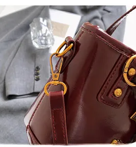 Detail of burgundy patent leather bucket bag with shiny gold metal hook and red stitching