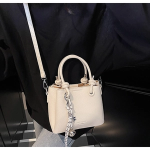 Détail du sac en cuir grainé beige avec charme en corde tressée et clochette