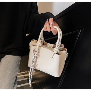Close-up of white lychee leather handbag with woven knot and key pendant detail